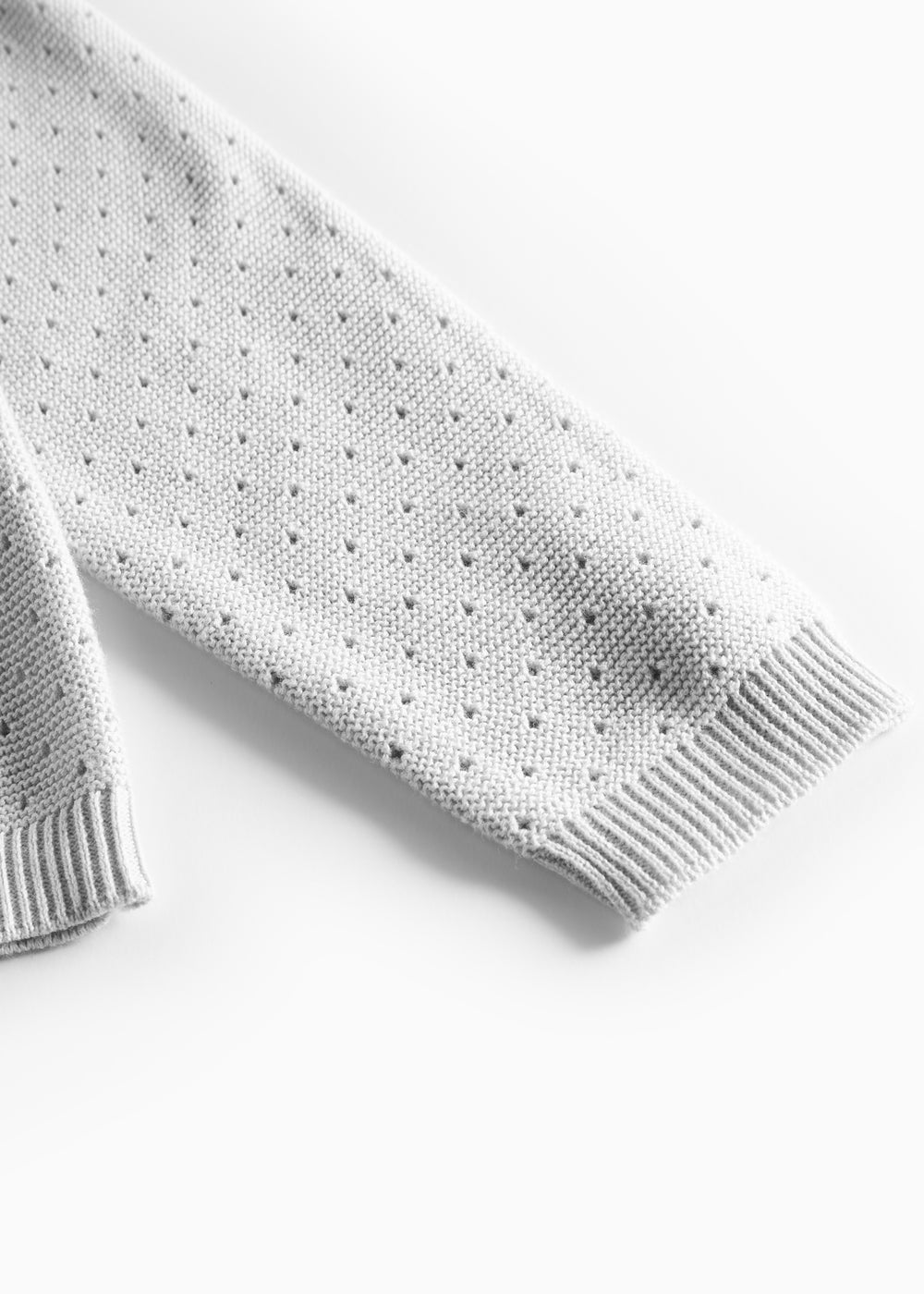 Detalje af ærme med hulmønster på grå strikbluse