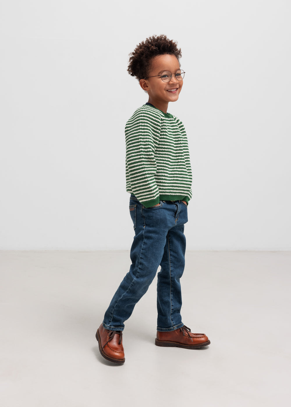 Dreng i grøn stribet striktrøje og jeans set fra siden