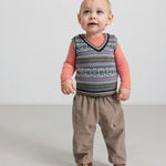Baby iført beige babyfløjl-sbukser og mønstret strikvest.