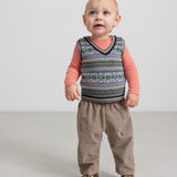 Baby iført beige babyfløjl-sbukser og mønstret strikvest.
