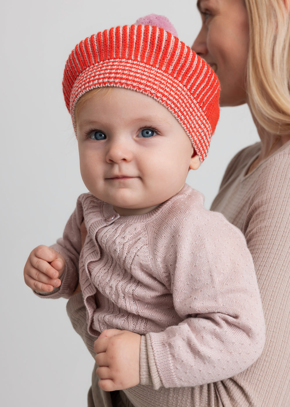 Baby med rød og hvid strikket beret og lyserød kvast