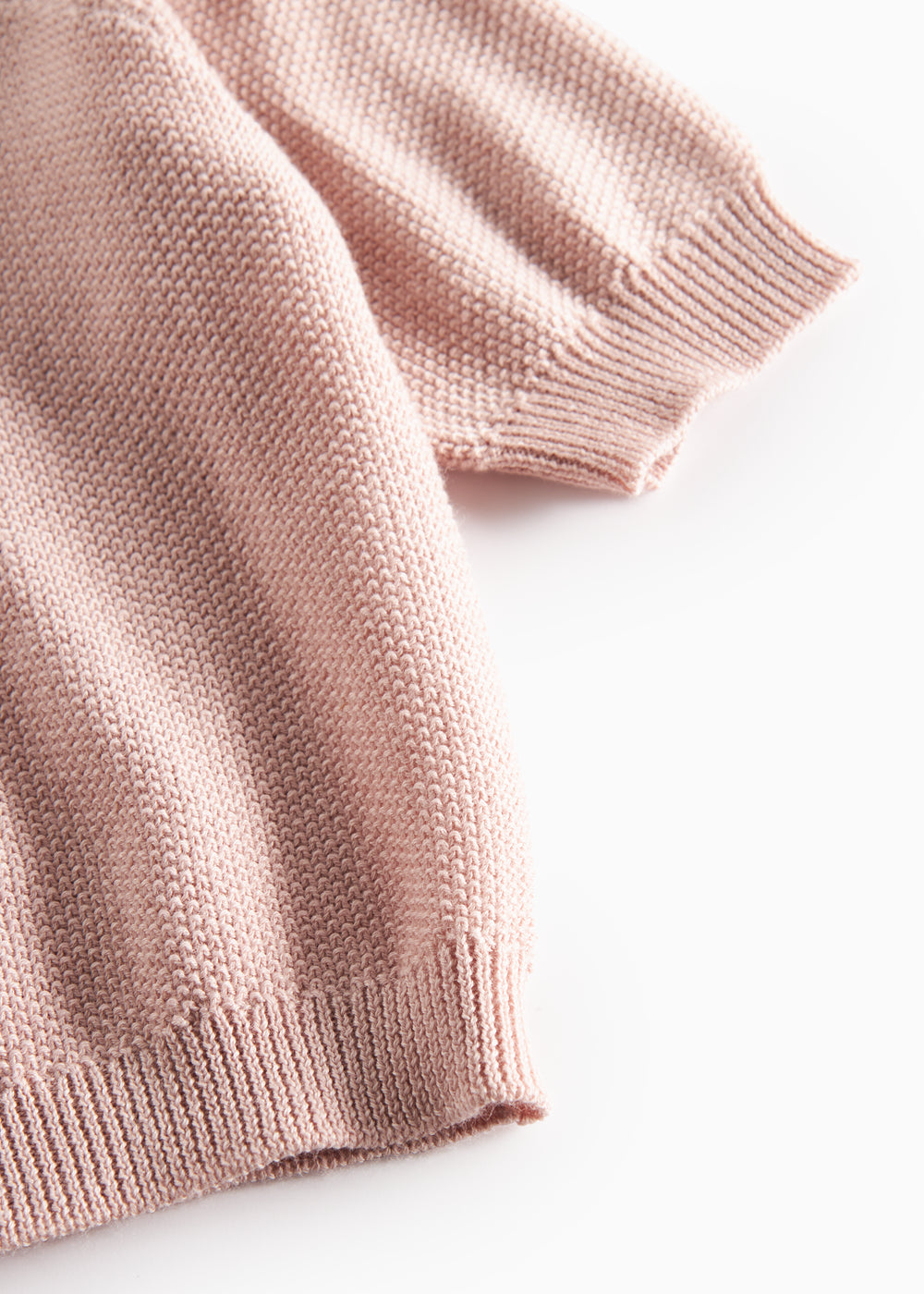 Nærbillede af ribkant ved ærme på lyserød strikket baby cardigan.