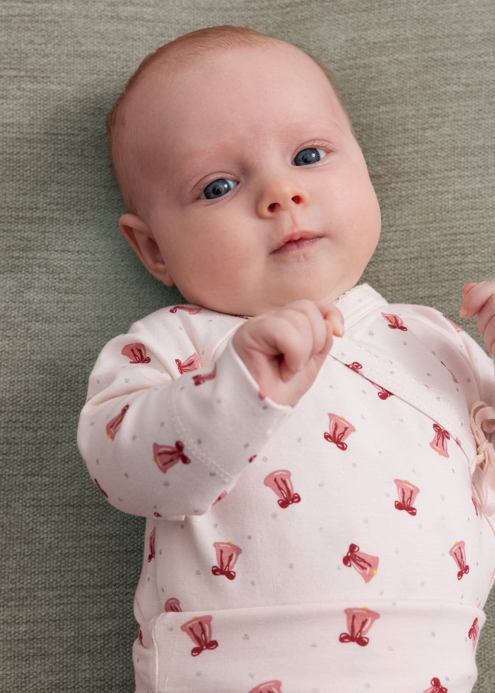 Baby med cremefarvet slå-om bluse og rødt juleklokkeprint