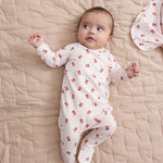 Baby iført cremefarvet heldragt med rødt juleklokkeprint liggende på tæppe