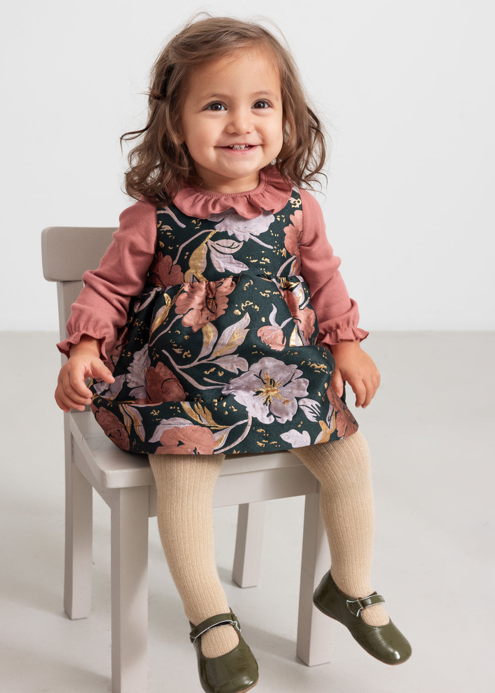 Baby iført mørkegrøn ærmeløs festkjole med blomsterprint og rosa bluse