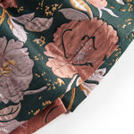 Nærbillede af mørkegrønt glansstof med blomsterprint og gyldne detaljer på festkjole til baby
