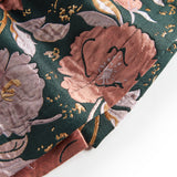 Nærbillede af mørkegrønt glansstof med blomsterprint og gyldne detaljer på festkjole til baby