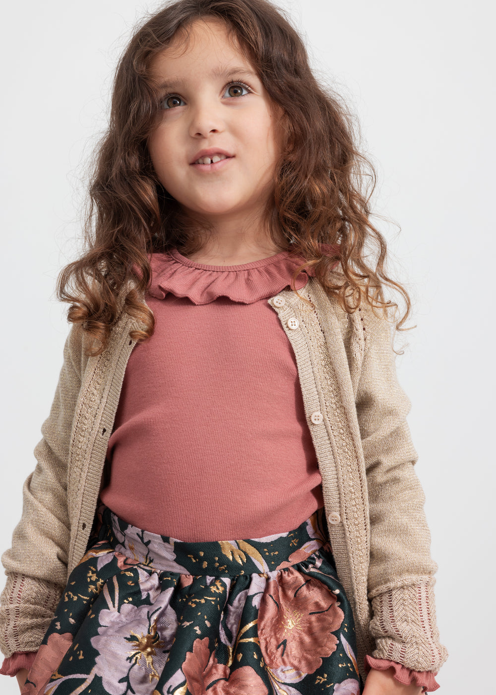 Pige iført beige cardigan med guldglimmer, rosa bluse og blomstretmønstret festnederdel til børn