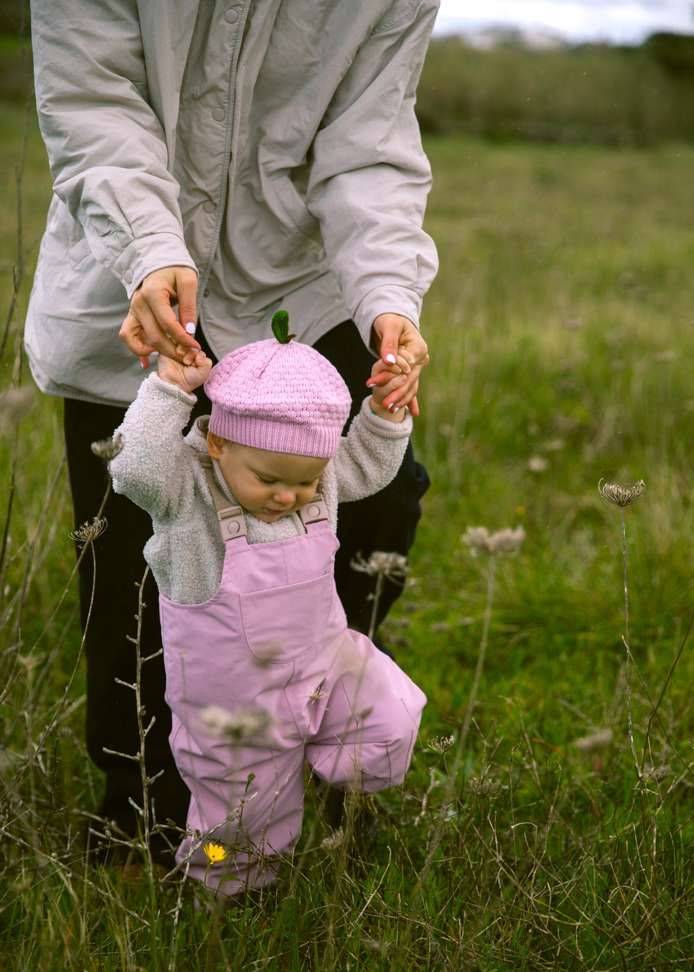 Baby iført lyserøde overtræksbukser og matchende hue gående støttet