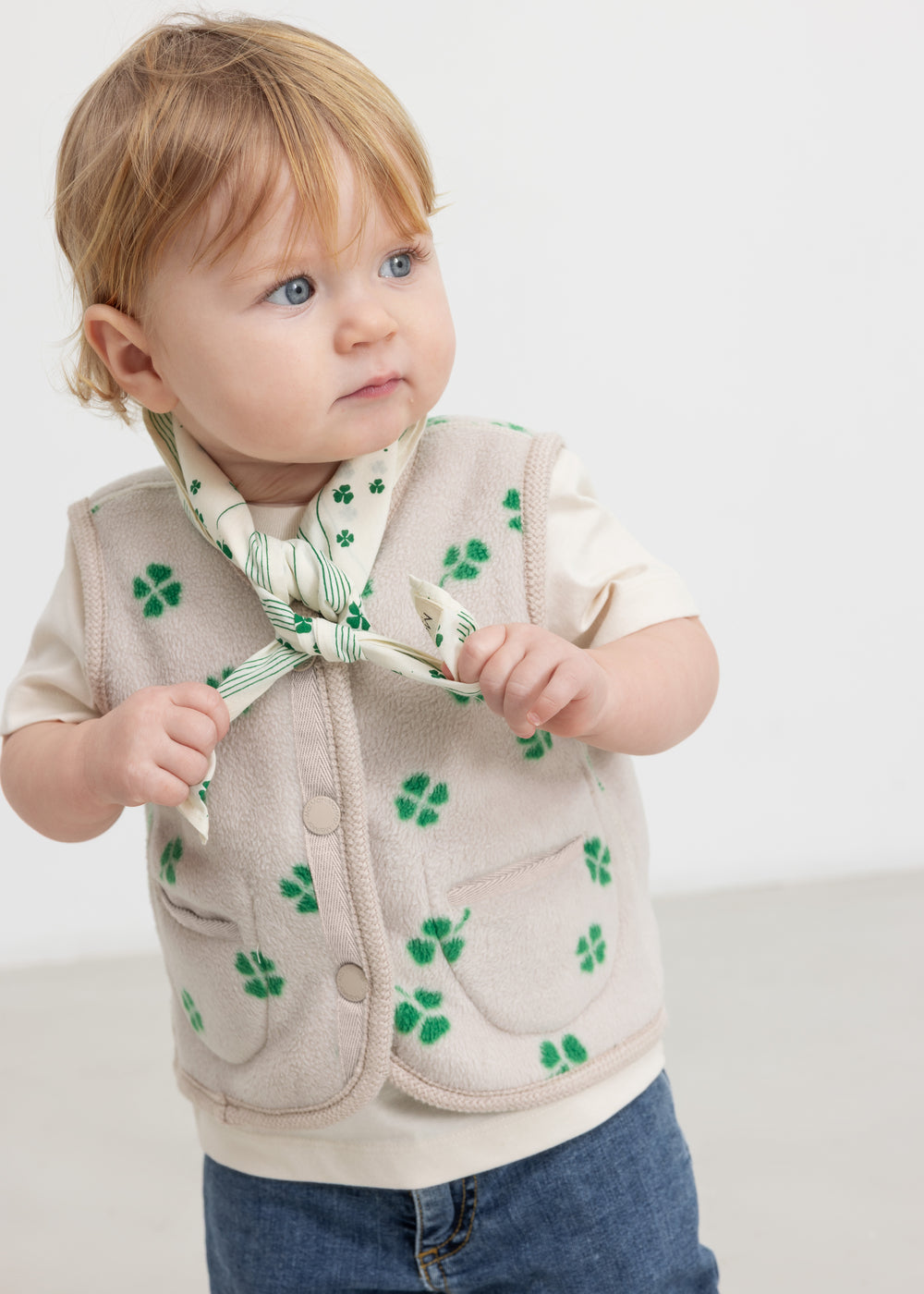 Baby iført beige vest med grønt kløverprint og knapper