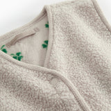 Detalje af beige teddy vest til børn med grønt kløverprint, trykknapper og blød struktur