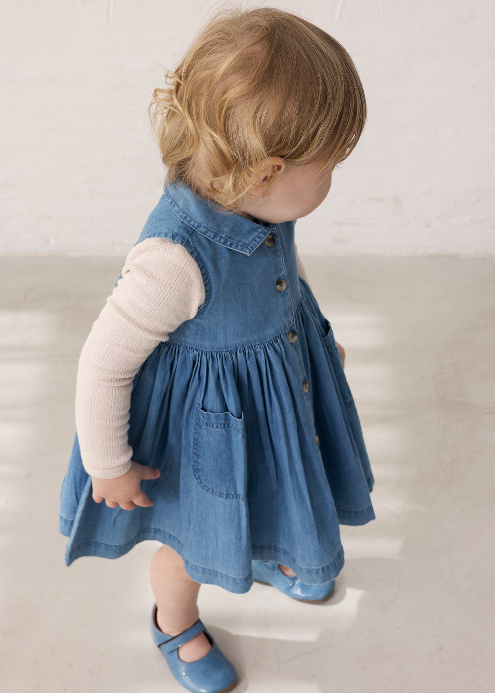 Barn iført blå denimkjole og langærmet body