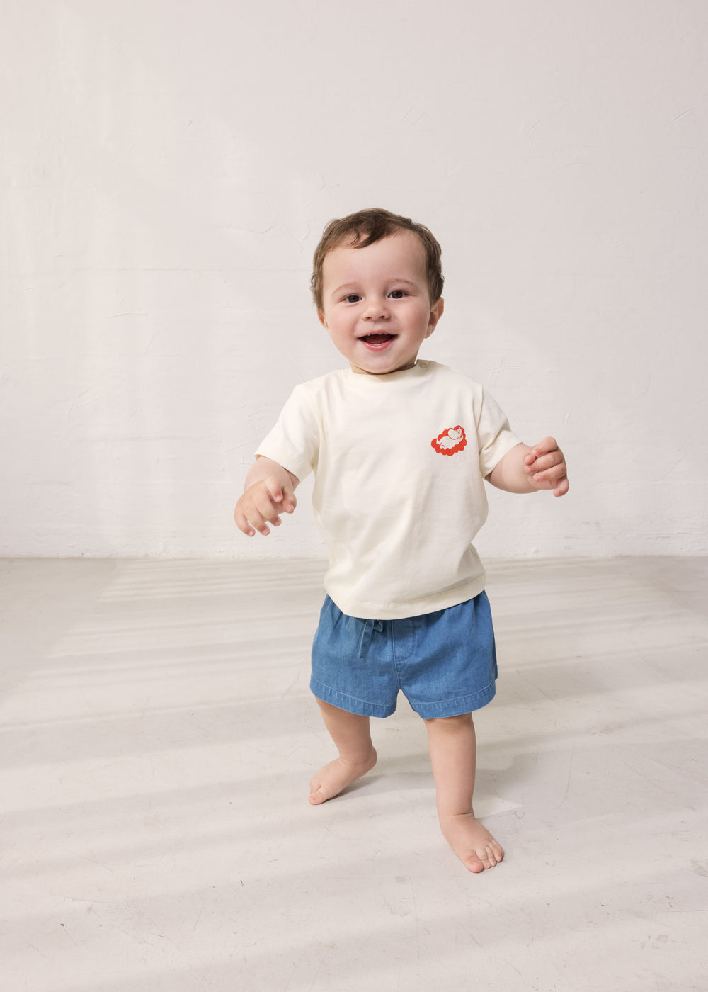 Baby iført råhvid T-shirt med Mumin-print og denim shorts