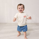 Baby iført råhvid T-shirt med Mumin-print og denim shorts
