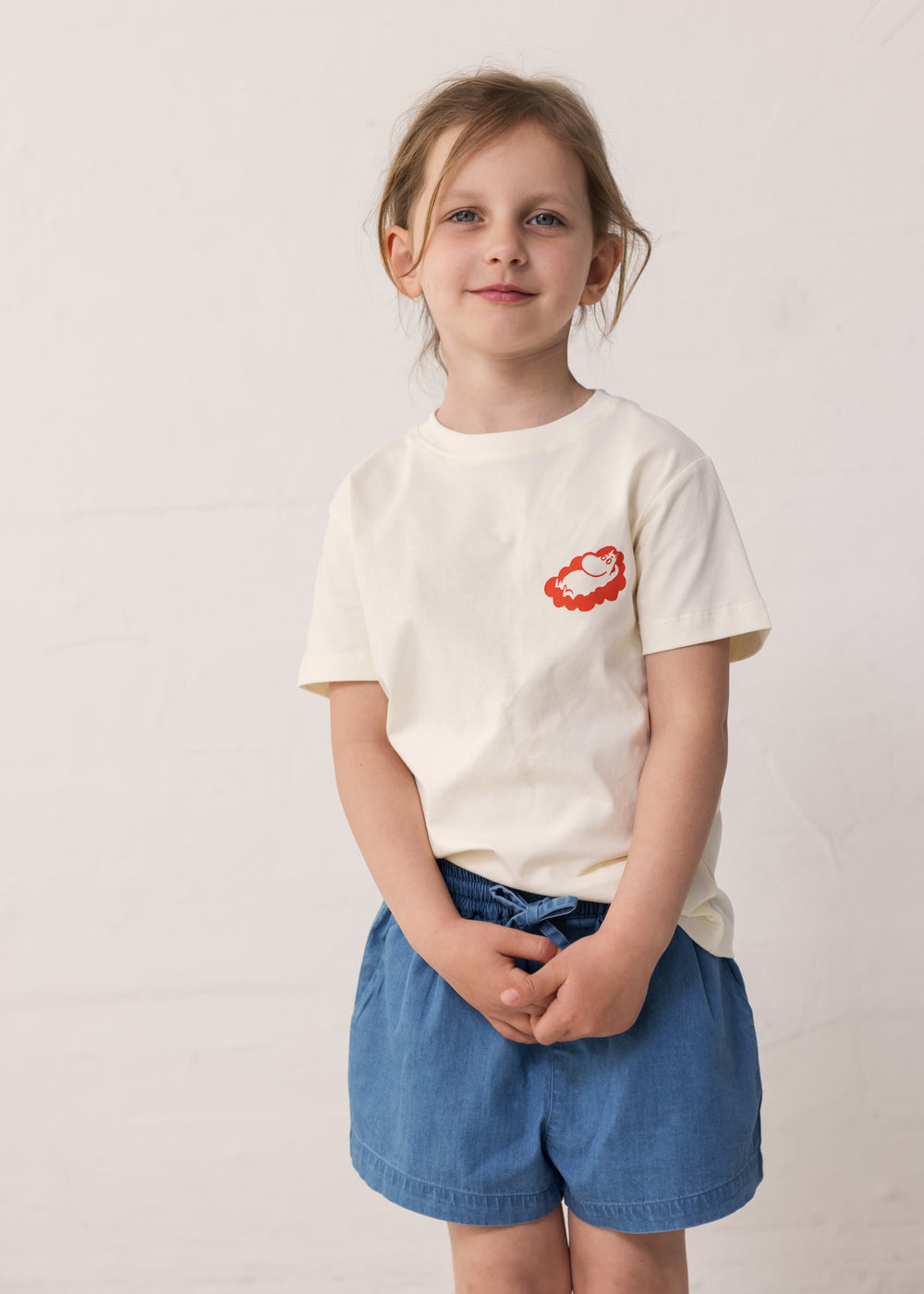 Barn iført råhvid T-shirt med Mumin-print og denimshorts
