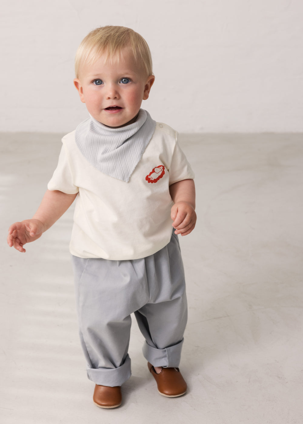 Baby iført råhvid T-shirt med Mumin-print og lyse bukser