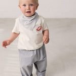 Baby iført råhvid T-shirt med Mumin-print og lyse bukser
