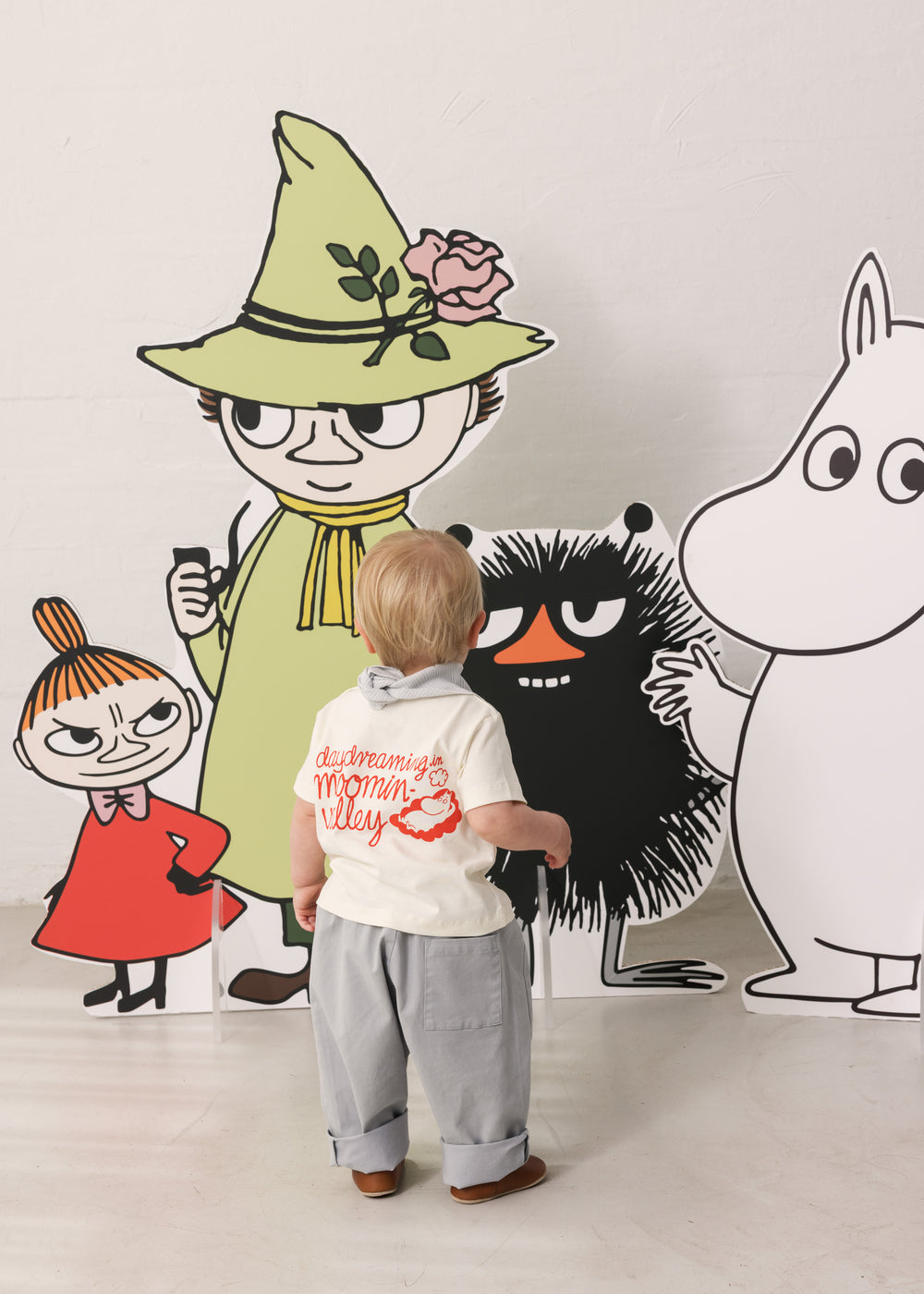 Baby iført råhvid T-shirt med Mumin-print og lyse bukser sammen med Moomin figurer