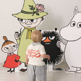 Baby iført råhvid T-shirt med Mumin-print og lyse bukser sammen med Moomin figurer