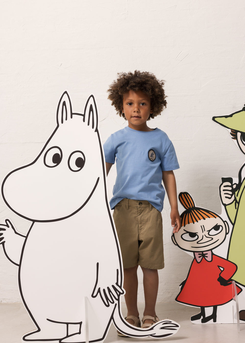 Barn iført lyseblå T-shirt og khakifarvede shorts sammen med Moomin figurer
