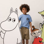 Barn iført lyseblå T-shirt og khakifarvede shorts sammen med Moomin figurer