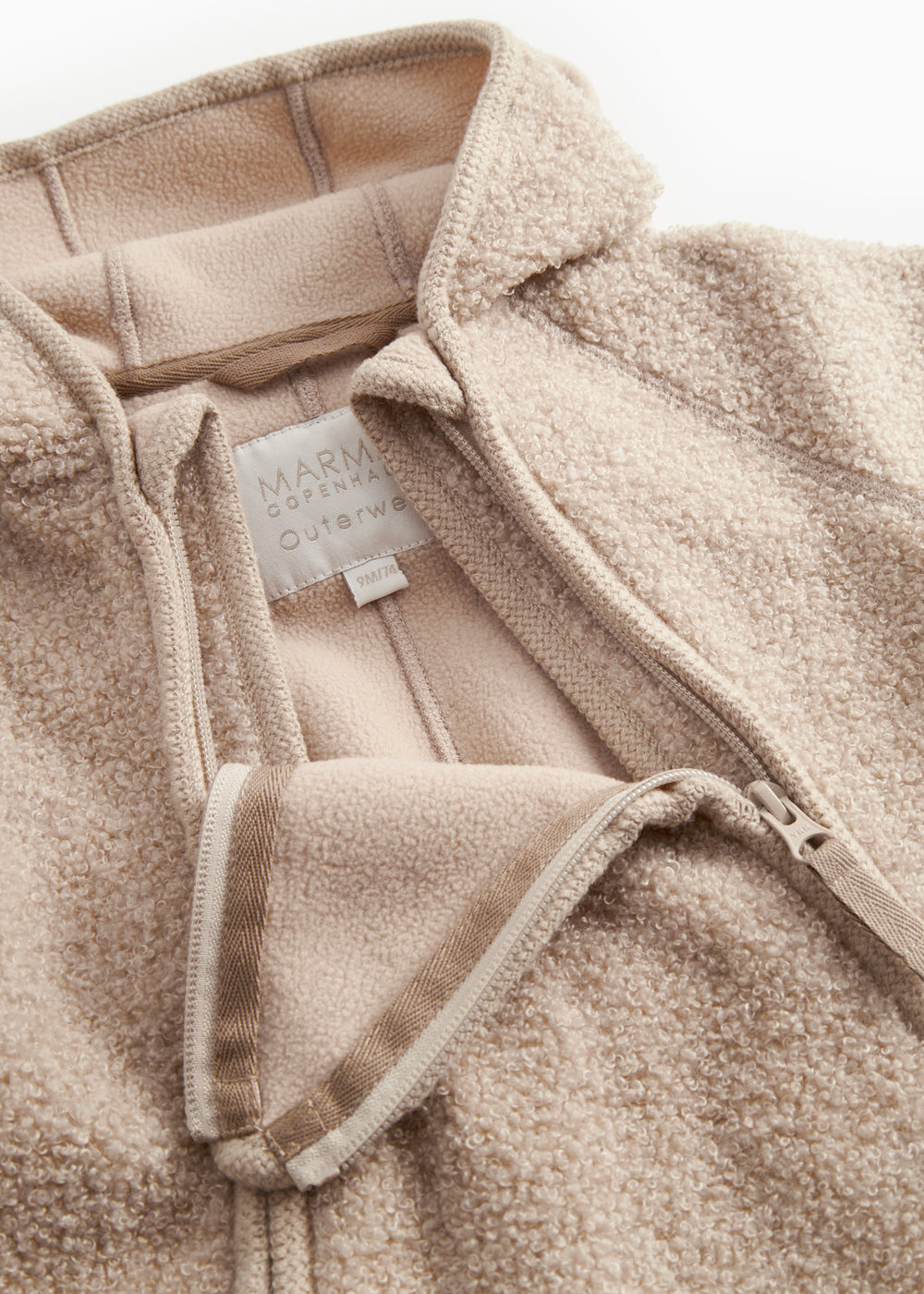 Beige teddyfleece heldragt med lynlås, synlig indvendig mærkning og snor