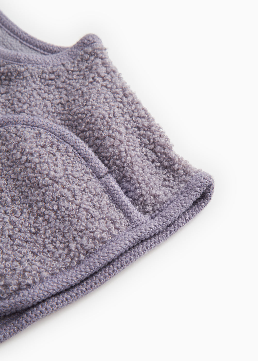 Lilla teddy-väst i blødt bouclé-look, tydelig kant og søm ved åbningen.