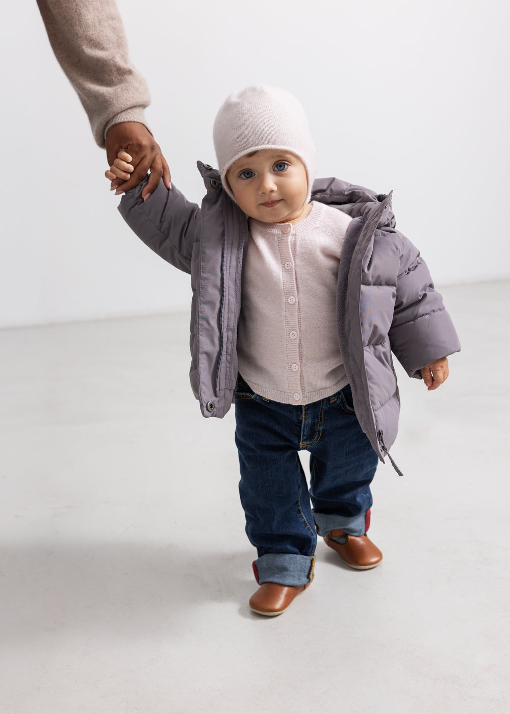 Lyserød babycardigan med knaplukning, synlig under grå vinterjakke.