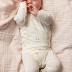 Cremet babysæt med små gule og blå prikker, baby med hænder ved ansigt