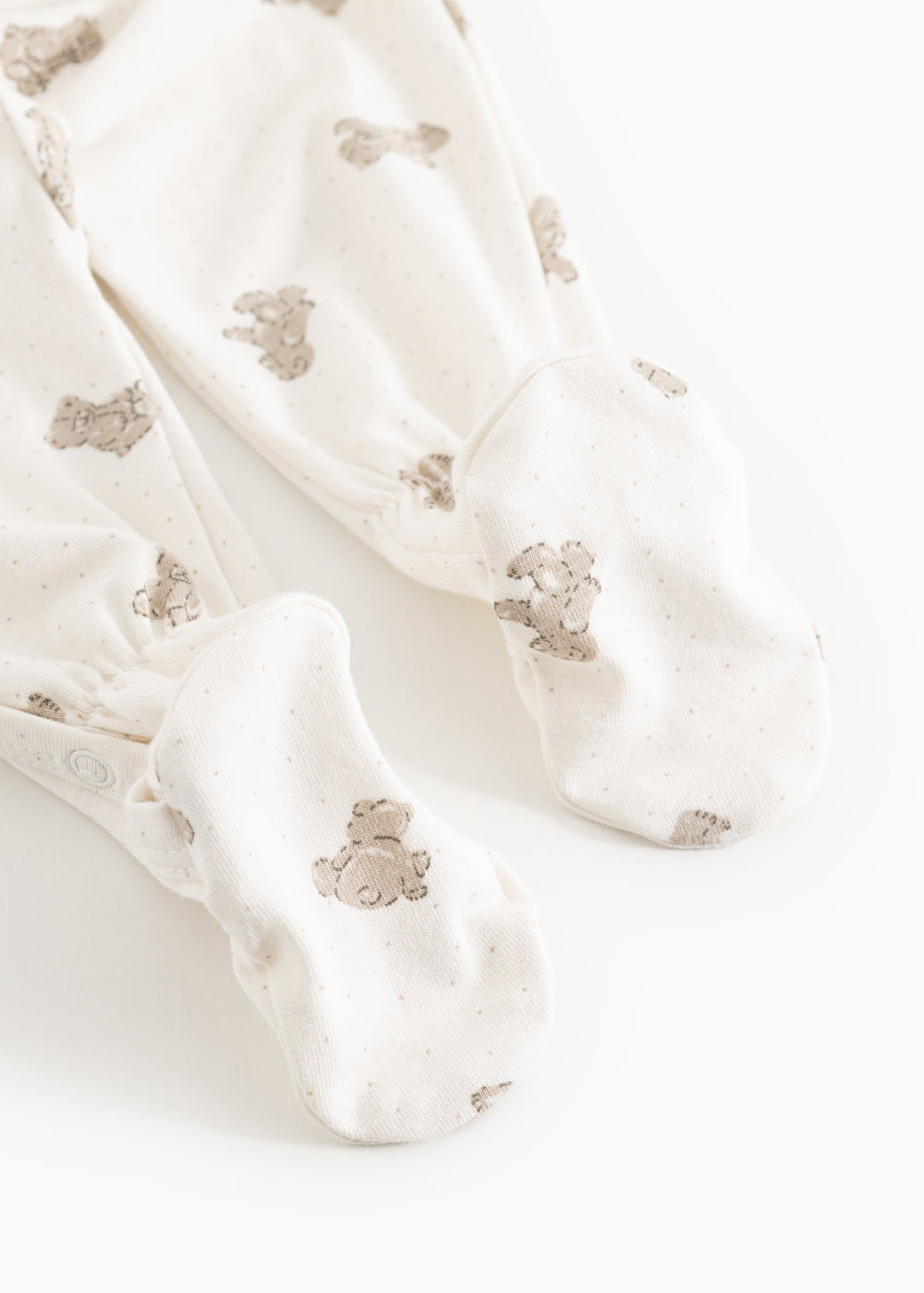 Hvid heldragt med beige teddybjørn-print og lange ben, set som close-up ved fødderne