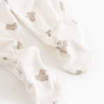 Hvid heldragt med beige teddybjørn-print og lange ben, set som close-up ved fødderne