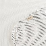 Tæppe med små sorte prikker og beige mærkeplade på hjørnet