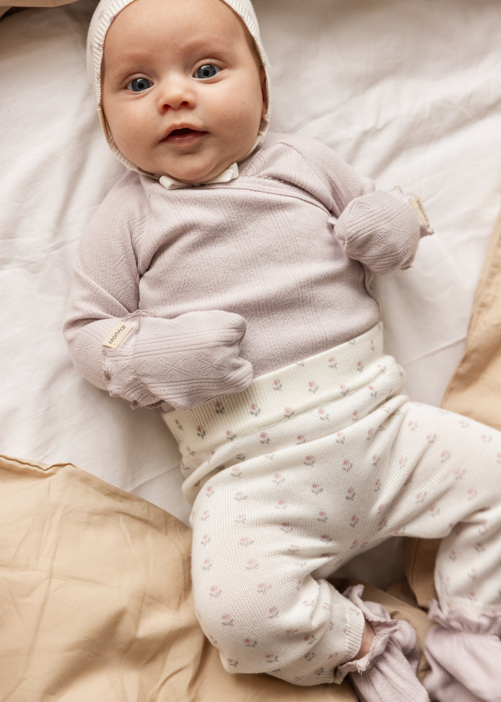 Baby iført lys lilla luffer i strik, elastisk manchet med dusk