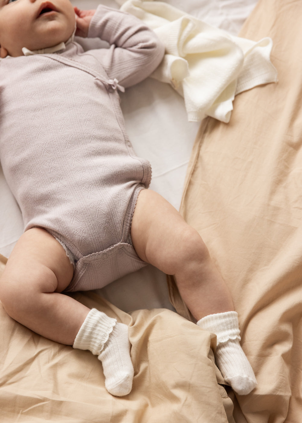 Baby-bodystocking i lys lilla med lange ærmer, synlige sømme ved ben