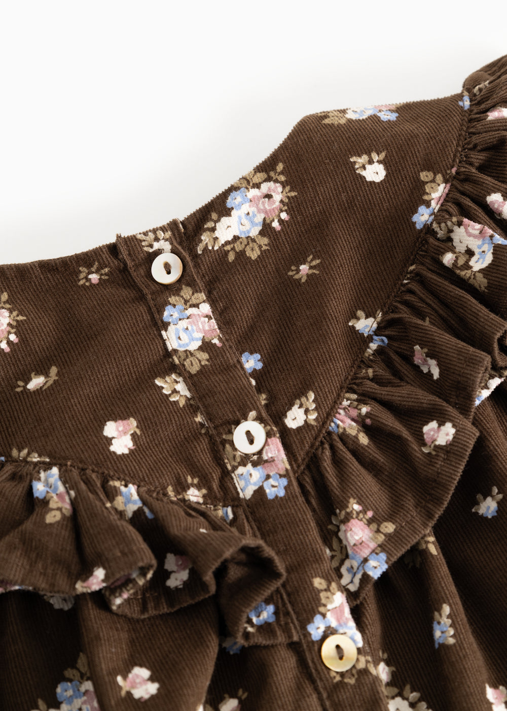 Detalje: Brun babybluse med flæsekrave, knapper ved hals og blomsterprint på ærmerne.