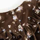 Detalje: Brun babybluse med flæsekrave, knapper ved hals og blomsterprint på ærmerne.