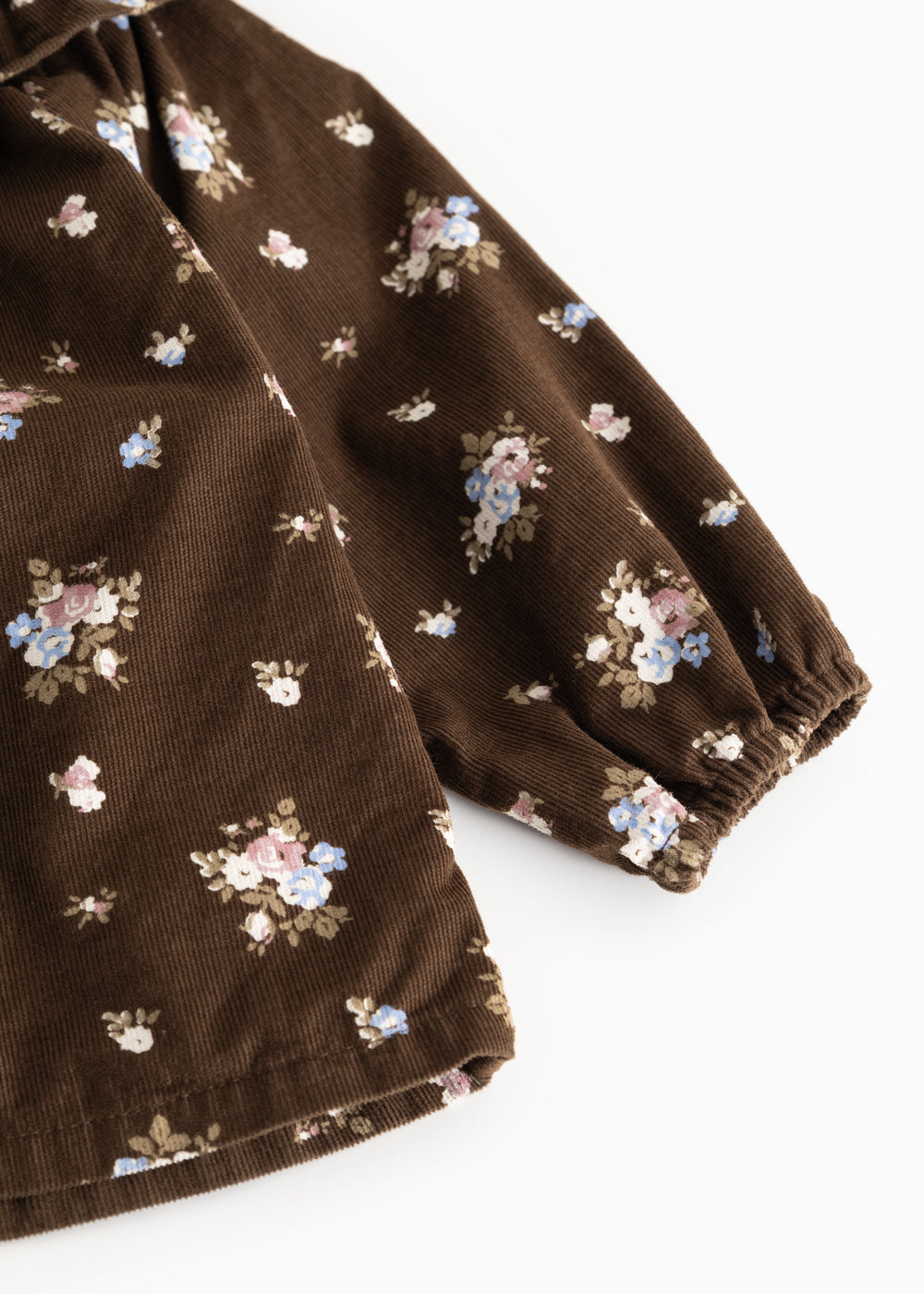 Brun babybluse med lange ærmer og fint blomstermønster; rynket kant ved manchet.