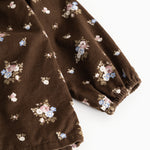 Brun babybluse med lange ærmer og fint blomstermønster; rynket kant ved manchet.