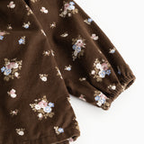 Brun babybluse med lange ærmer og fint blomstermønster; rynket kant ved manchet.