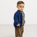 Blå strikket cardigan på baby i sideprofil med sorte ribkanter.