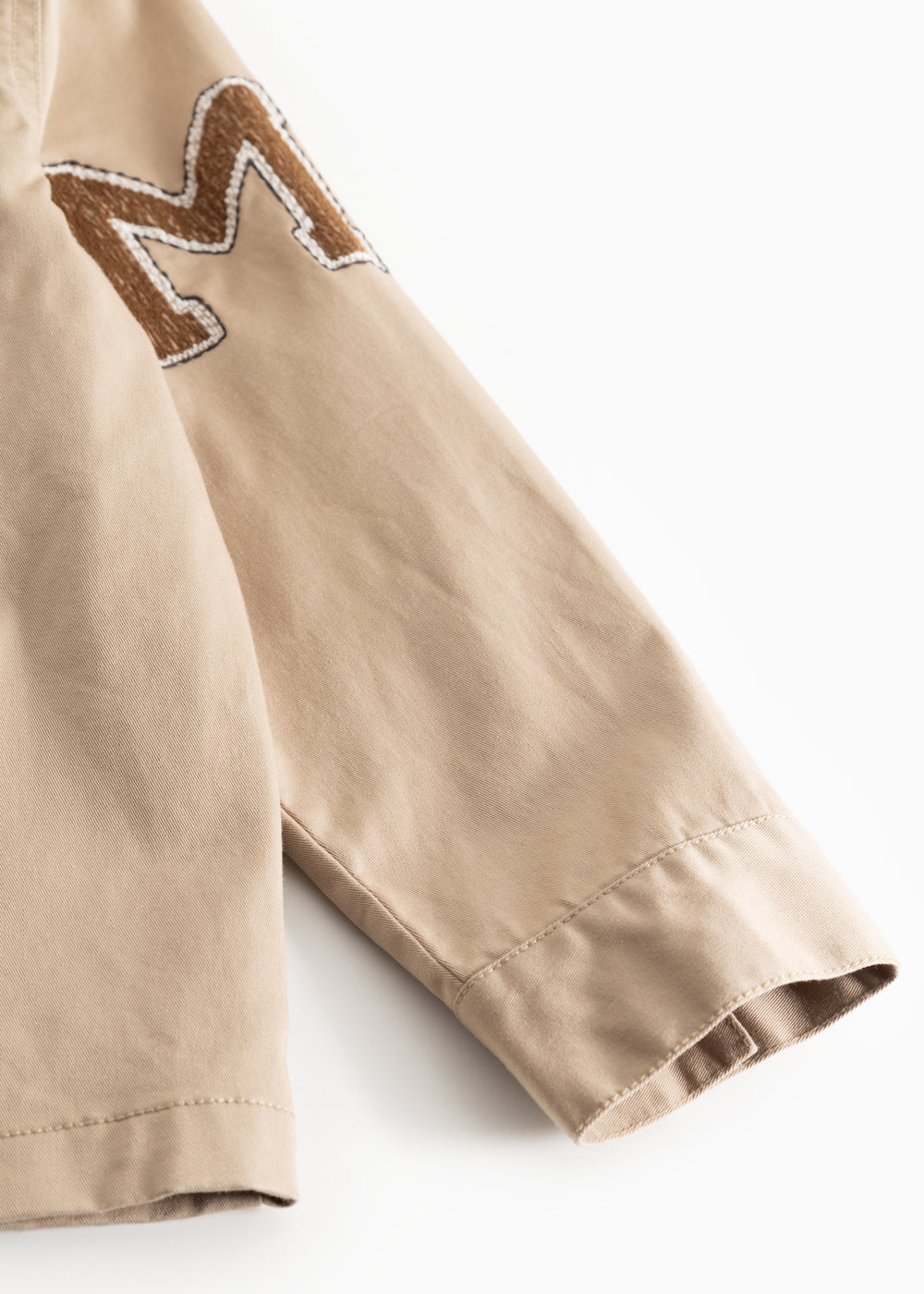 Beige jakkeærme med broderet mærkepatch ved skulderen