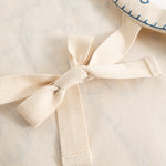 Naturfarvet forklæde med bindebånd og stofsløjfe foran, synlige teksturer