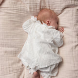 Lys svøb om baby, løse rynkefolder foran og hænder ved kroppen