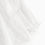 Hvid babybluse med flæsekant ved ærme og let tekstureret stof