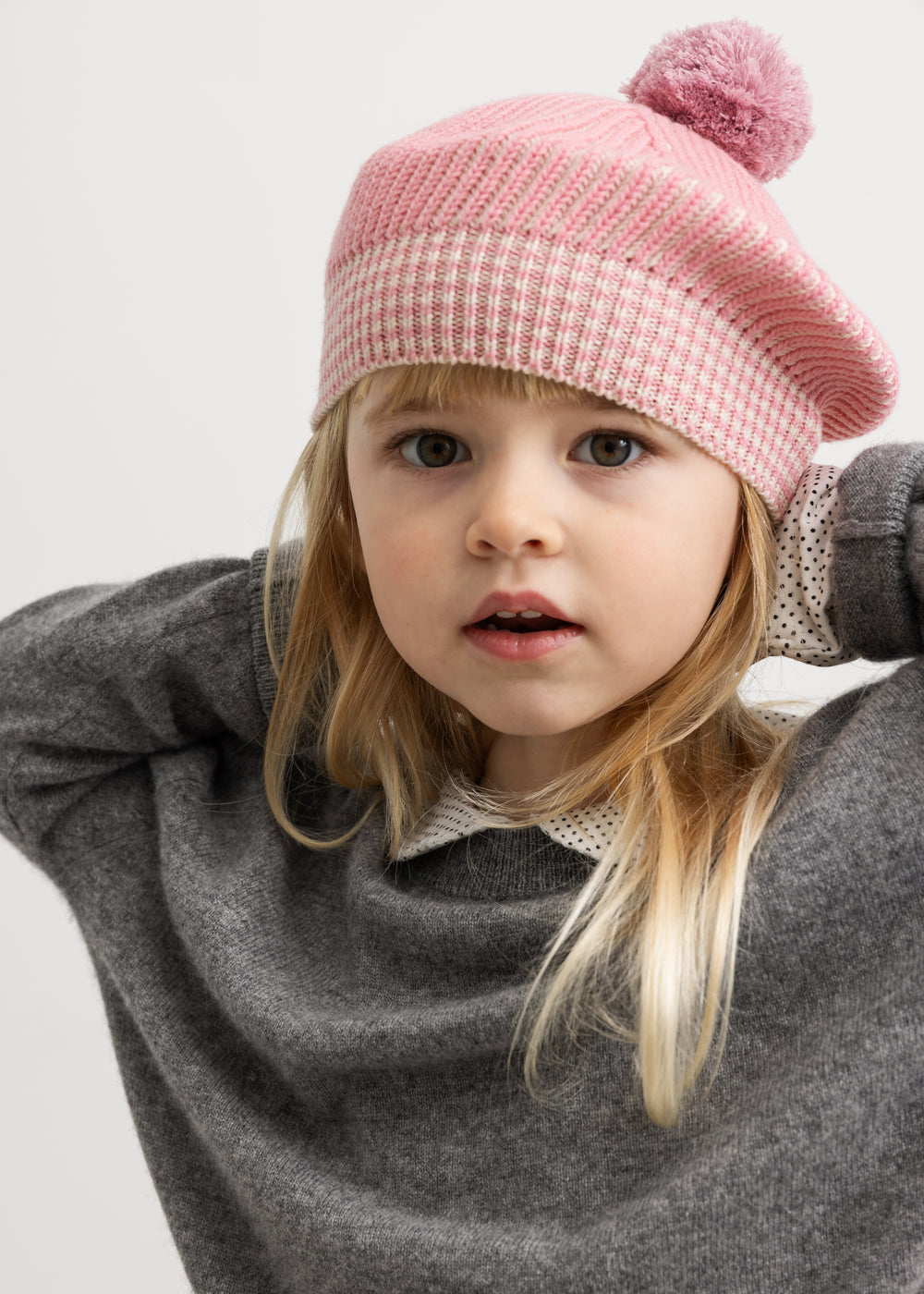 Lyserød strikhue med pompon, båret af barn med lyst hår.