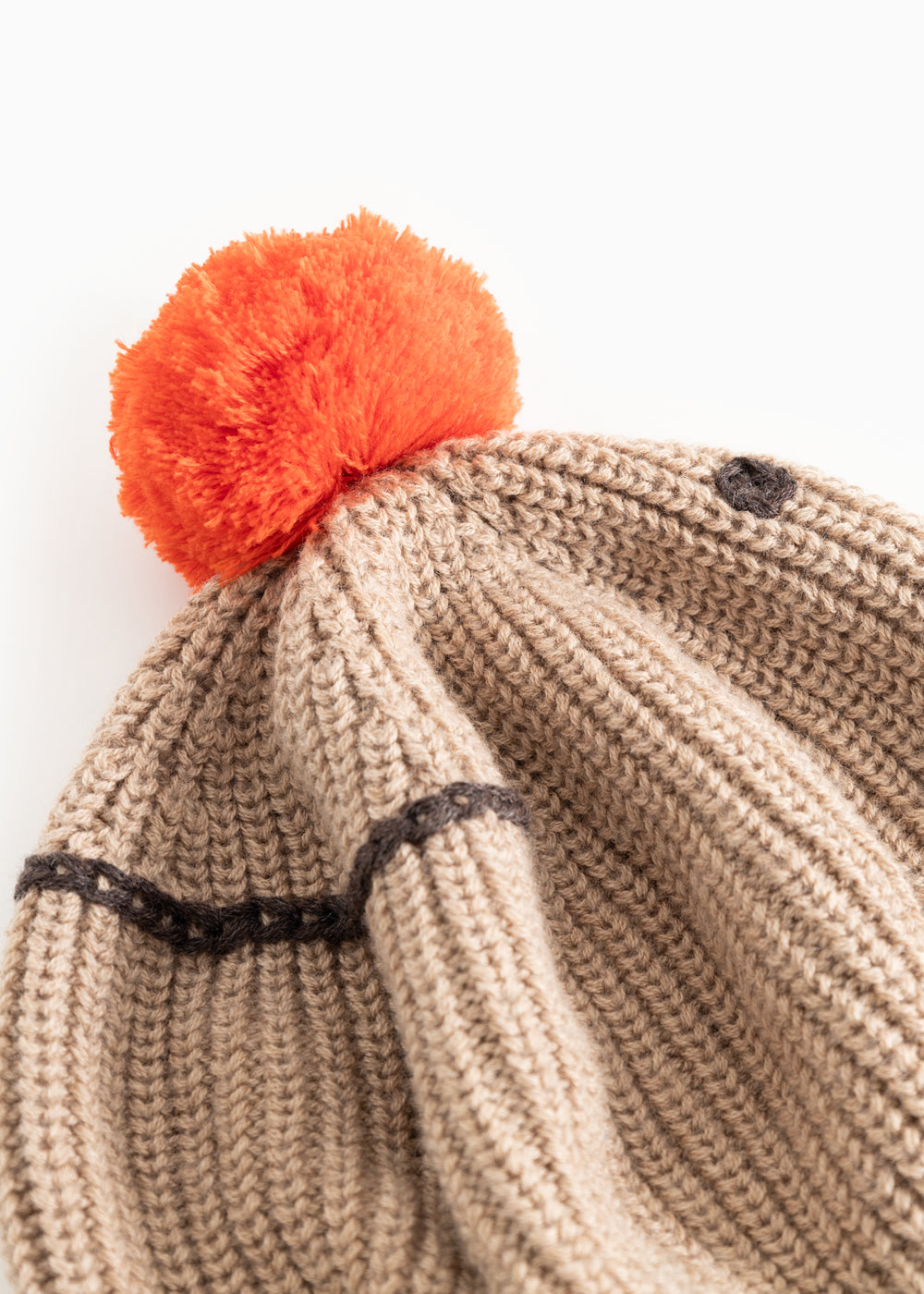 Detalje: Beige strikhue med sort mønsterkant og orange kvast
