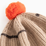 Detalje: Beige strikhue med sort mønsterkant og orange kvast