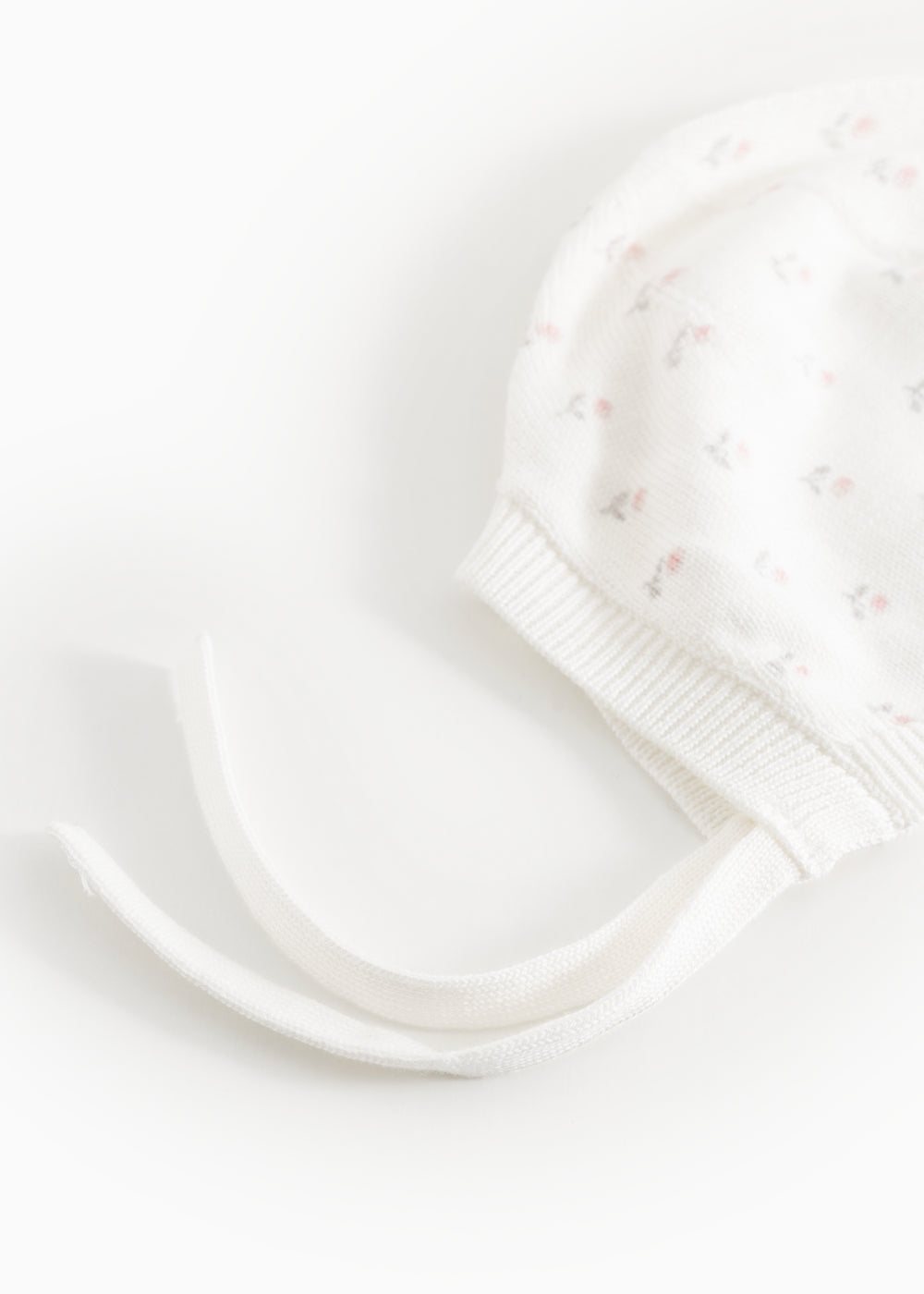 Hvid babyhue med små blomsterprint, ribkant og lange bindesnore