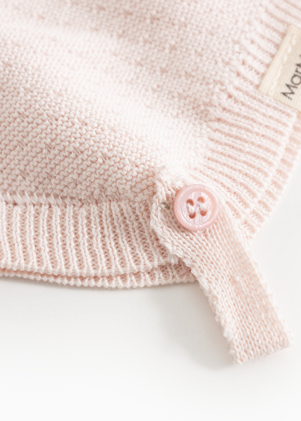 Detalje af rosa strikhue: ribkant og lyserød trykknap