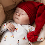 Baby i hvid heldragt med musiker-mønster og rød hue med pompon.